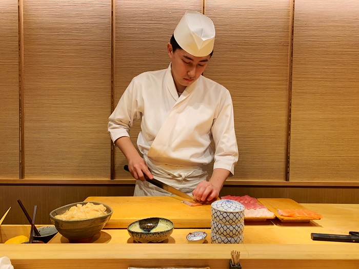 The sushi chef slicing into fish